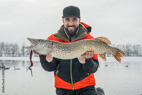Winter fishing. Happy fisherman with pike fish at snowy lake