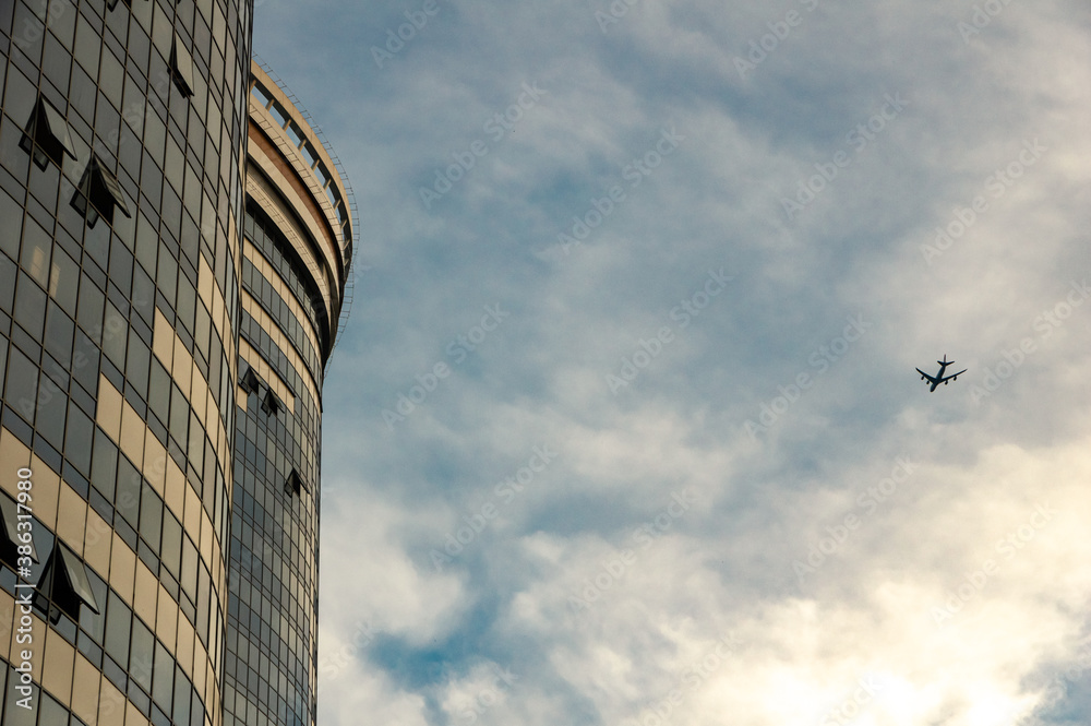 Obraz premium Bottom view of high-rise buildings with a mirrored facade with the silhouette of a flying plane against the sky.