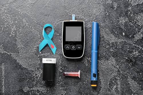 Awareness ribbon with glucometer, blood sample and syringe on dark background. Diabetes concept