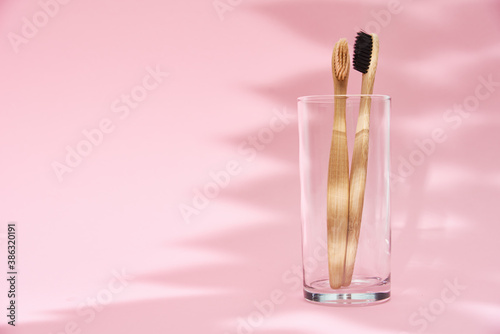 Bamboo toothbrushes in the glass and leaf shadows on pink background