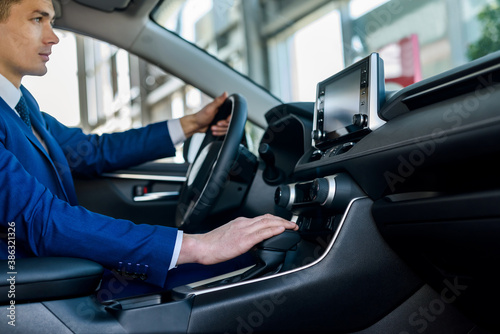 Young and happy businessman sitting in new car in showroom