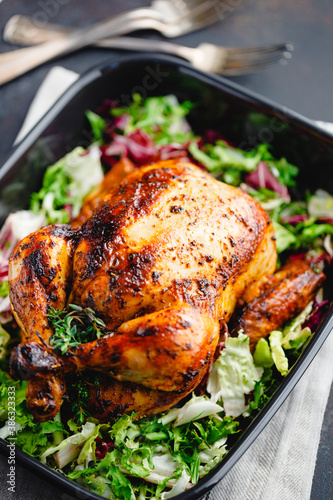 Top view of a whole roasted chicken served with fresh salad in black pan. Thanksgiving or family dinner celebration cooking concept.