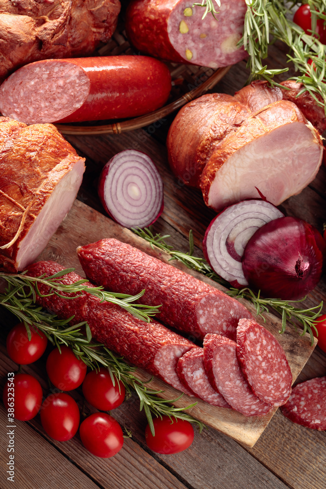Food tray with delicious salami, ham, fresh sausages, tomato, and rosemary.