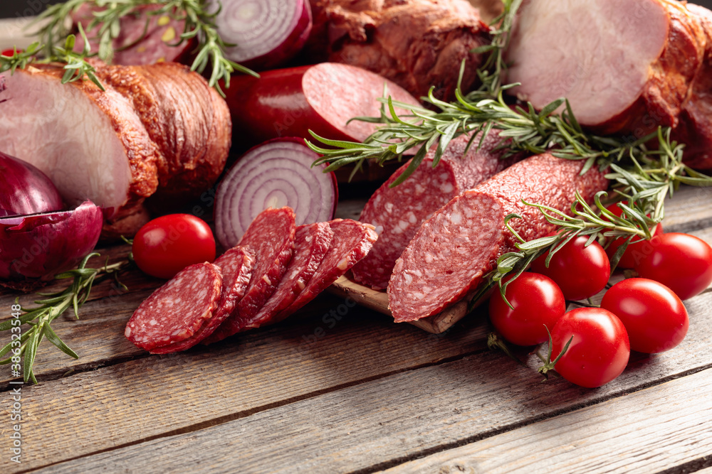 Food tray with delicious salami, ham, fresh sausages, tomato, and rosemary. Food tray with delicious salami, ham, fresh sausages, tomato, and rosemary.