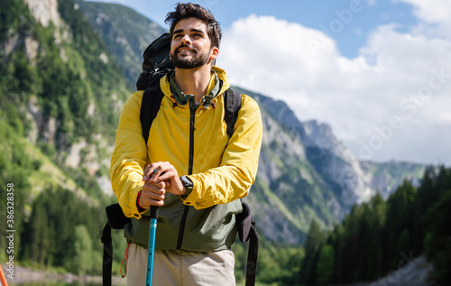Hiker young man with backpack and trekking poles looking at the mountains in outdoor