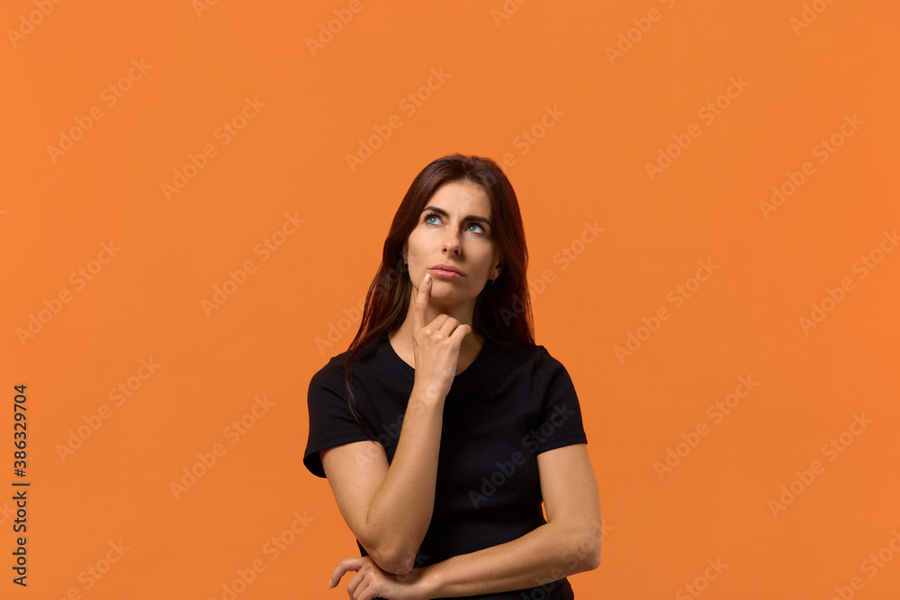 I need to find a solution. Attractive caucasian woman in black t-shirt looks pensively upwards. With puzzled expression thinking about something. Isolated over an orange wall I need to find a solution. Attractive caucasian woman in black t-shirt looks pensively upwards. With puzzled expression thinking about something. Isolated over an orange wall