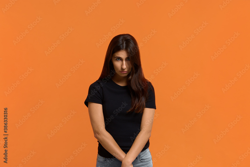Obraz premium Forgive me. Miserable sad pleading caucasian woman in black t-shirt says sincere please, makes apology, keeps arms together in front of, begs with upset expression. Isolated over an orange wall