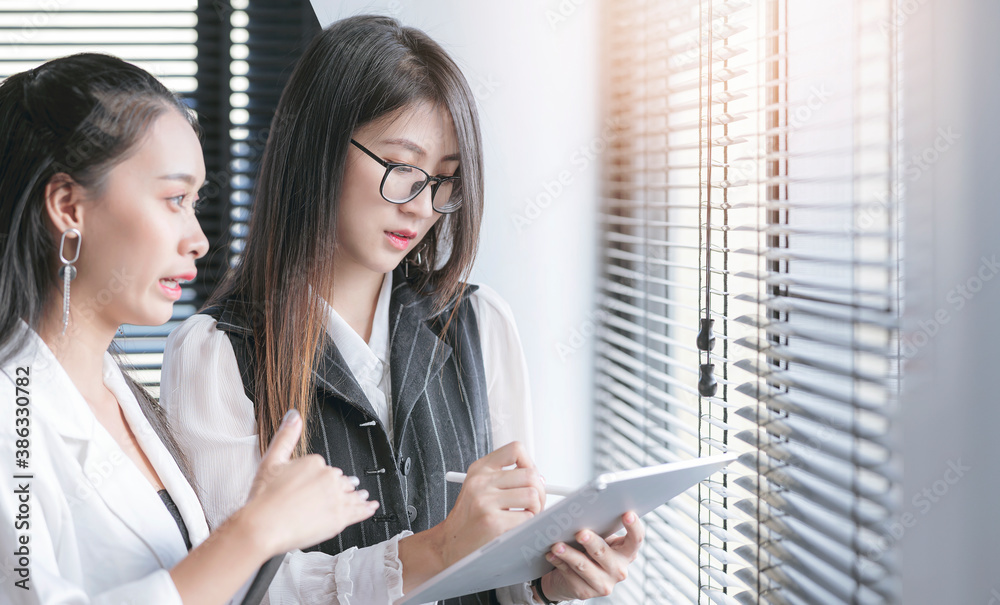 Fototapeta premium Two businesswoman using tablet and discussing about business while standing at office room.