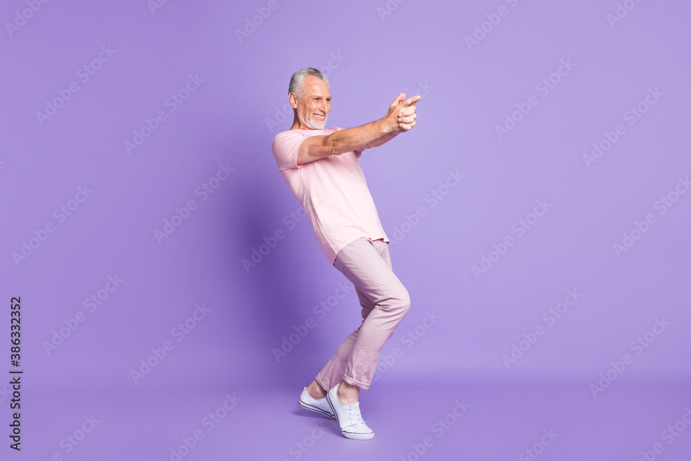 Full length profile photo of pensioner man close fingers gun play wear pink t-shirt pants sneakers isolated purple color background Full length profile photo of pensioner man close fingers gun play wear pink t-shirt pants sneakers isolated purple color background