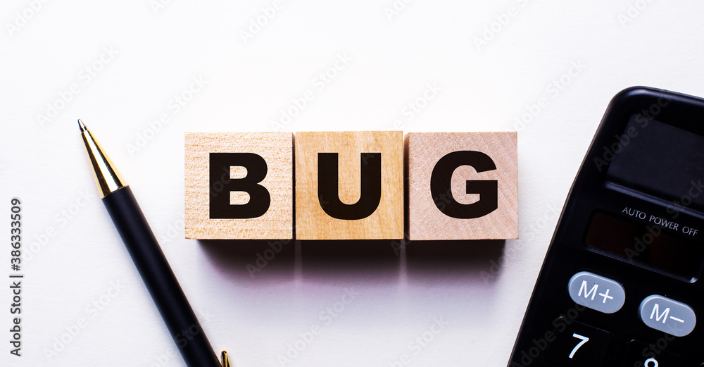 BUG is written on wooden cubes between a pen and a calculator on a light background. BUG is written on wooden cubes between a pen and a calculator on a light background.