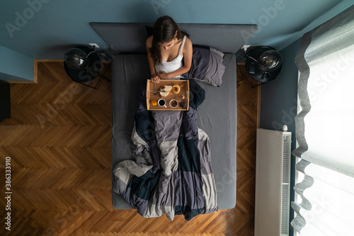 Image from above of attractive woman eating breakfast alone on the bed. photo