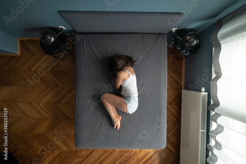 Image from above of depressive woman feeling alone at the bed.