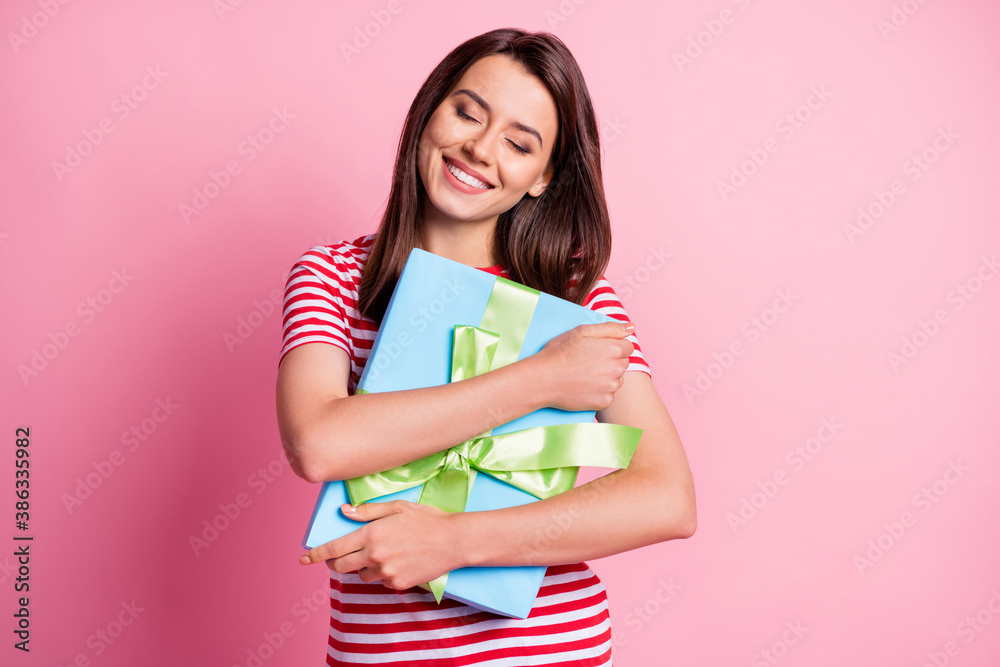 Photo portrait of happy birhtday girl hugging embracing wrapped present with closed eyes isolated on pastel pink color background Photo portrait of happy birhtday girl hugging embracing wrapped present with closed eyes isolated on pastel pink color background