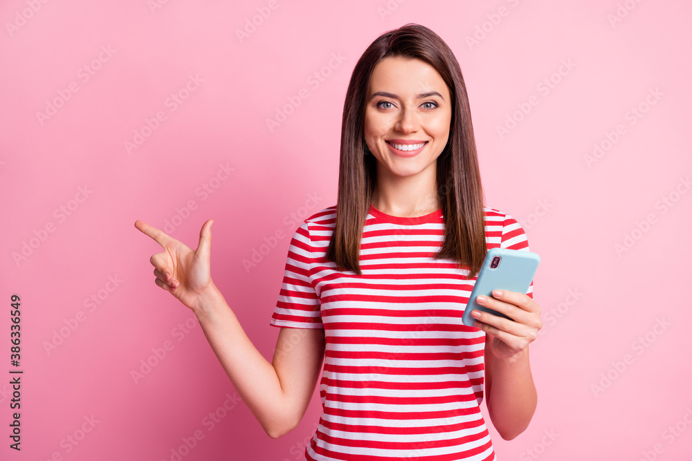 Photo portrait of girl keeping cellphone pointing at blank space isolated on pastel pink color background Photo portrait of girl keeping cellphone pointing at blank space isolated on pastel pink color background