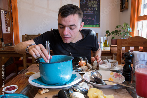 Jeune homme se servant dans une marmite bleue un plat traditionnel appelé le curanto dans un restaurant chilien  photo