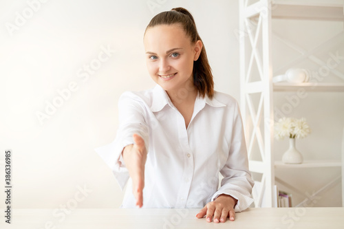 Job interview. Professional career. Promotion growth. Presentable cheerful female HR in white shirt smiling greeting candidate with handshake at light modern workspace with copy space background.