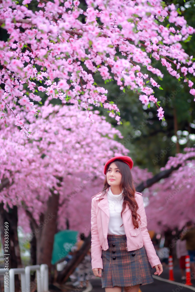 A traveler hipster woman sightseeing wear a red hat and a smooth leather dress with beautiful sakura cherry blossoms tree full blooming in pink color in the park on a spring day. A traveler hipster woman sightseeing wear a red hat and a smooth leather dress with beautiful sakura cherry blossoms tree full blooming in pink color in the park on a spring day.