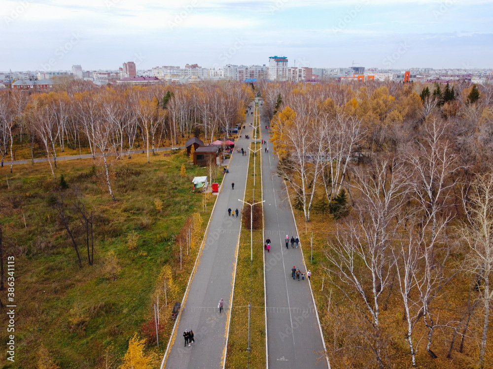 Alley in the park of the 30th anniversary of the Komsomol from a height. People walk on a day off in the park in the fall. Central alley in the park of Omsk