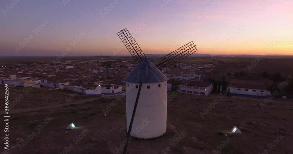 Aerial view Beautiful sunset over white cylindrical towers and pointed roofs of old Spanish windmills on background with Campo de Criptana, Spain
