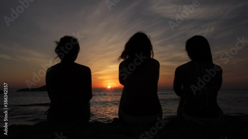 Silhouette of three friends at sea in golden and beautiful sunset. . Young women on holidays summer evening. Happy people watching the sunset, Ibiza Cafe del Mar, Spain photo