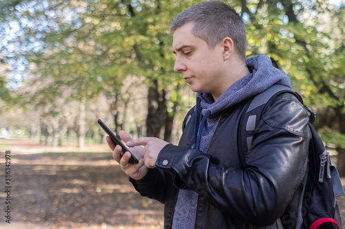 A man in a leather jacket looks at the phone in the middle of the forest. Social media immersion, orienteering, and phone stress concept