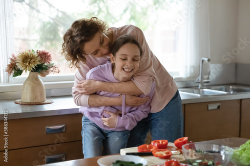 Loving Caucasian mom hug play with teen daughter cooking tasty salad for dinner at home kitchen. Caring happy mother enjoy day with teenage girl child, laugh have fun preparing healthy food together.