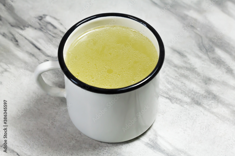Chicken broth in a white mug on a gray marble table. Meat broth. Healthy food. Broth for the disease. Close-up. Chicken broth in a white mug on a gray marble table. Meat broth. Healthy food. Broth for the disease. Close-up.