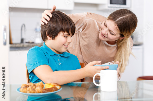 Portrait of young woman and tweenage boy having breakfast in kitchen at home