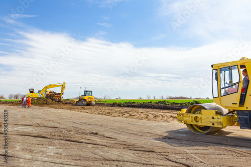 Excavator is loading a truck with ground on building site, road roller compact soil