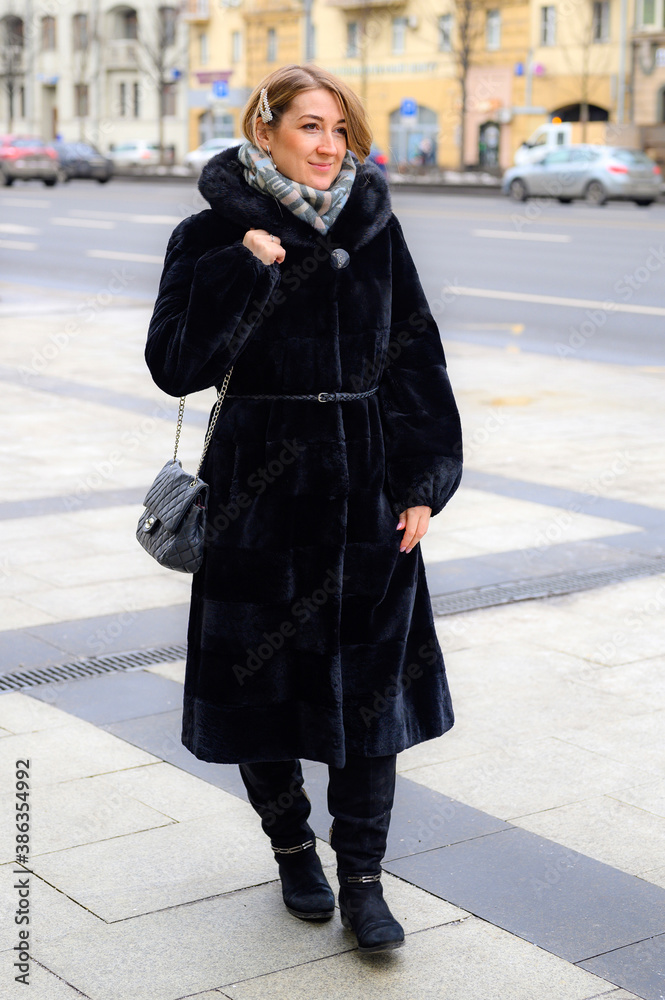 a beautiful young happy woman in fashionable winter fur coat walks along a city street a beautiful young happy woman in fashionable winter fur coat walks along a city street