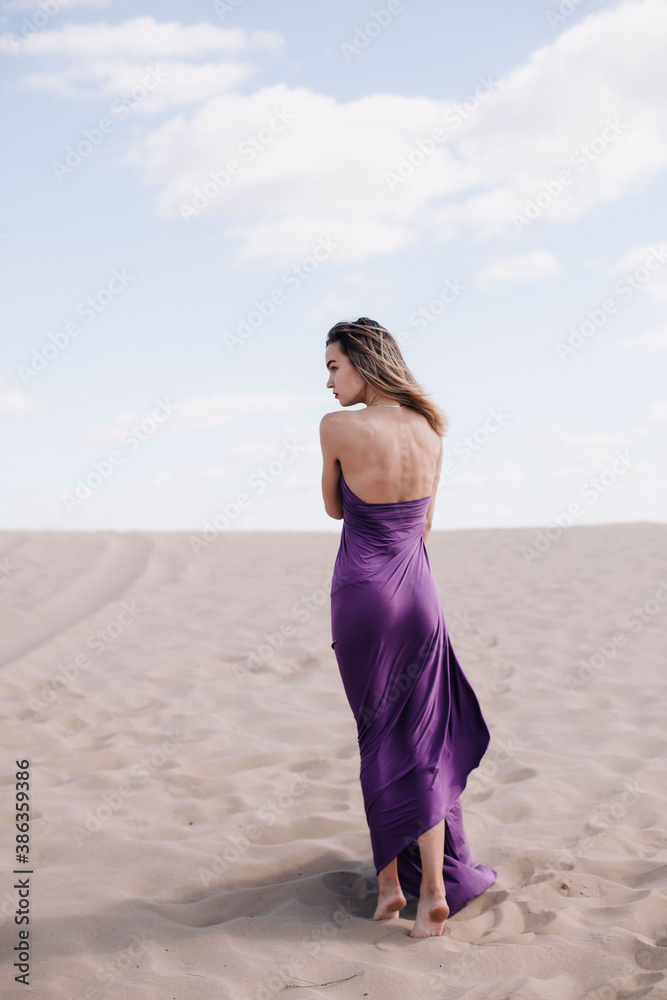 A young, slender girl in a beige dress with purple cloth in her hands posing in the desert in the wind A young, slender girl in a beige dress with purple cloth in her hands posing in the desert in the wind