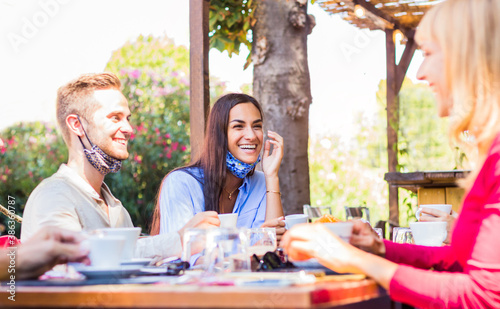 Happy friends with face mask drinking espresso at coffee house - New normal lifestyle concept of young people having fun at restaurant 