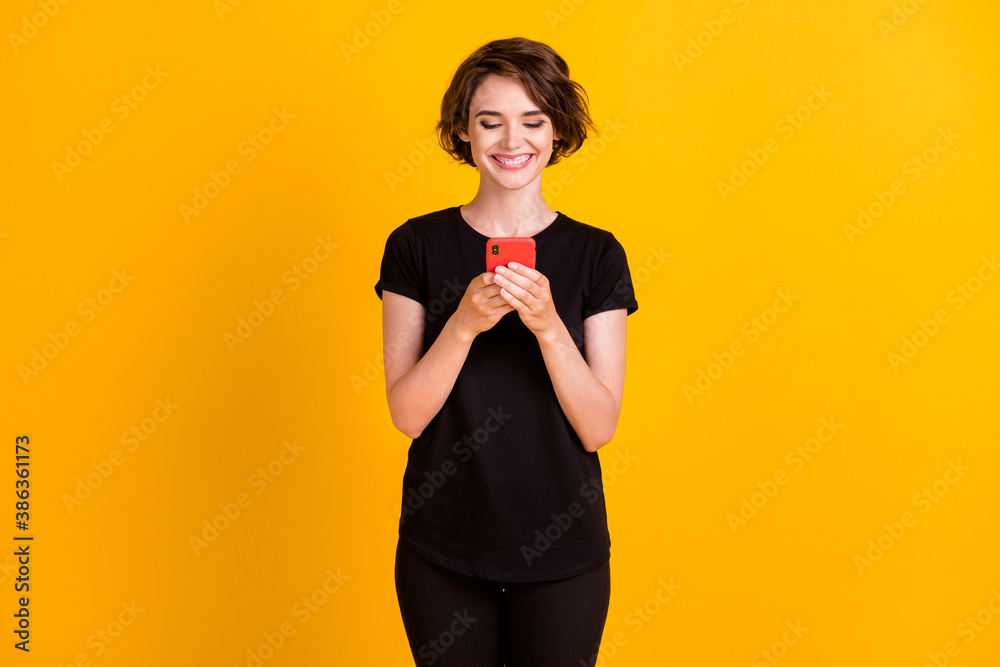 Portrait of attractive focused cheerful girl holding in hands using device chatting isolated over bright yellow color background Portrait of attractive focused cheerful girl holding in hands using device chatting isolated over bright yellow color background
