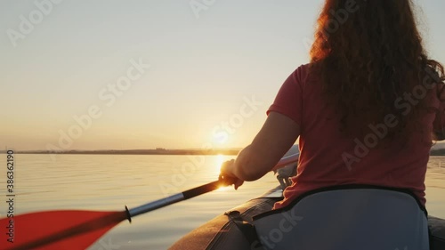 Happy young woman paddling on an inflatable kayak with her dog Jack Russell Terrier on water of sea against beautiful orange sunset slow motion. Family Sports. Summer. Travel. Tourism. Relax. Freedom