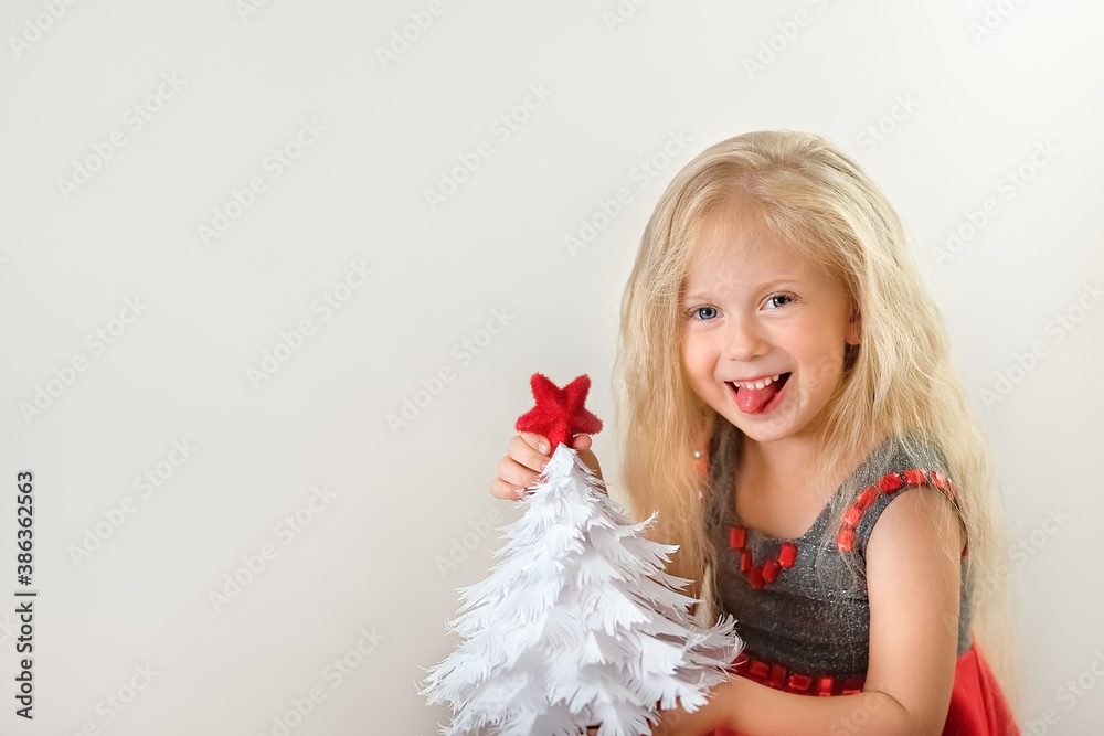 Little smiling girl with white paper christmas tree and red star in her hands Little smiling girl with white paper christmas tree and red star in her hands