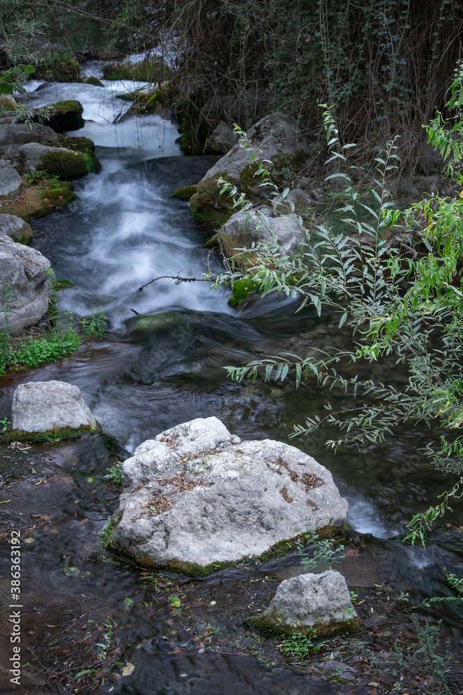 Fast running mountain river with mossy boulders and rocks at cloudy day on long exposure.