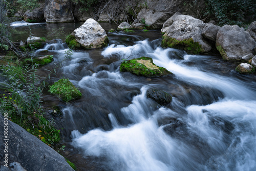 Fast running mountain river with mossy boulders and rocks at cloudy day on long exposure.