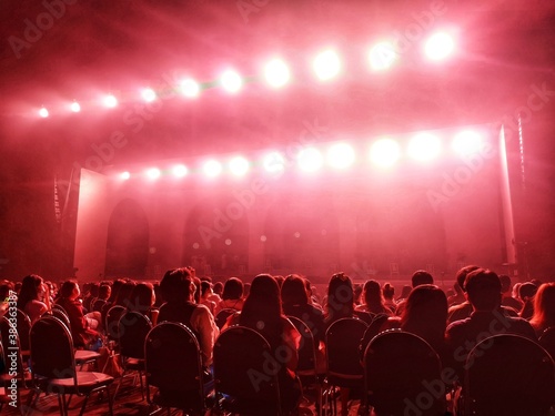 Blurred crowd at social distancing concert venue in Thailand during the coronavirus (covid-19) : Silhouette happy people sitting in front of stage with bright laser light beam.The New Normal