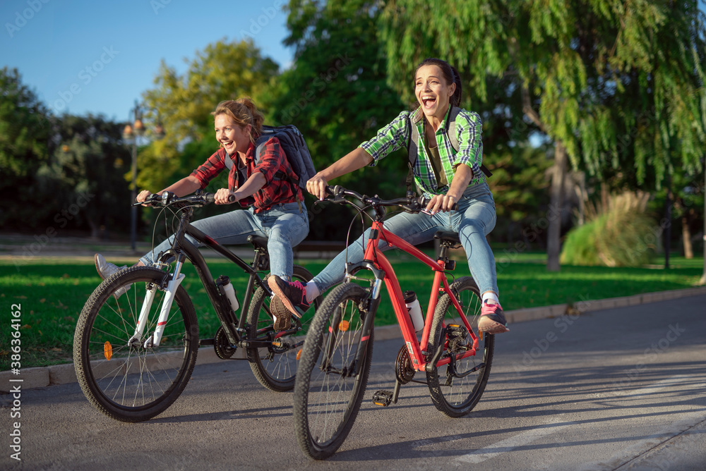 Two pretty young caucasian girls having fun on bicycles along the street. Best friends enjoying a day on bikes. Sunny summer evening
