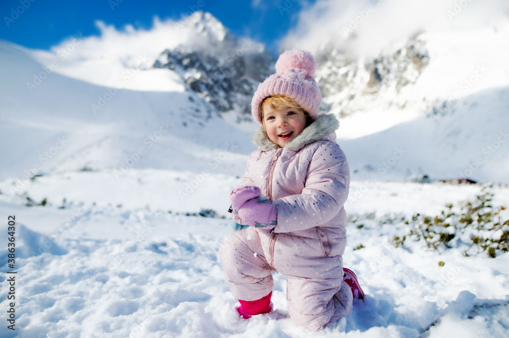 Portrait of cheerful small girl lying in snow in winter nature, playing.