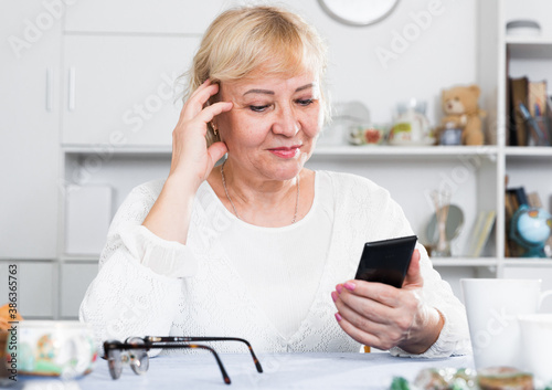 Mature woman sitting at table at home and looking at smartphone in her hands. photo