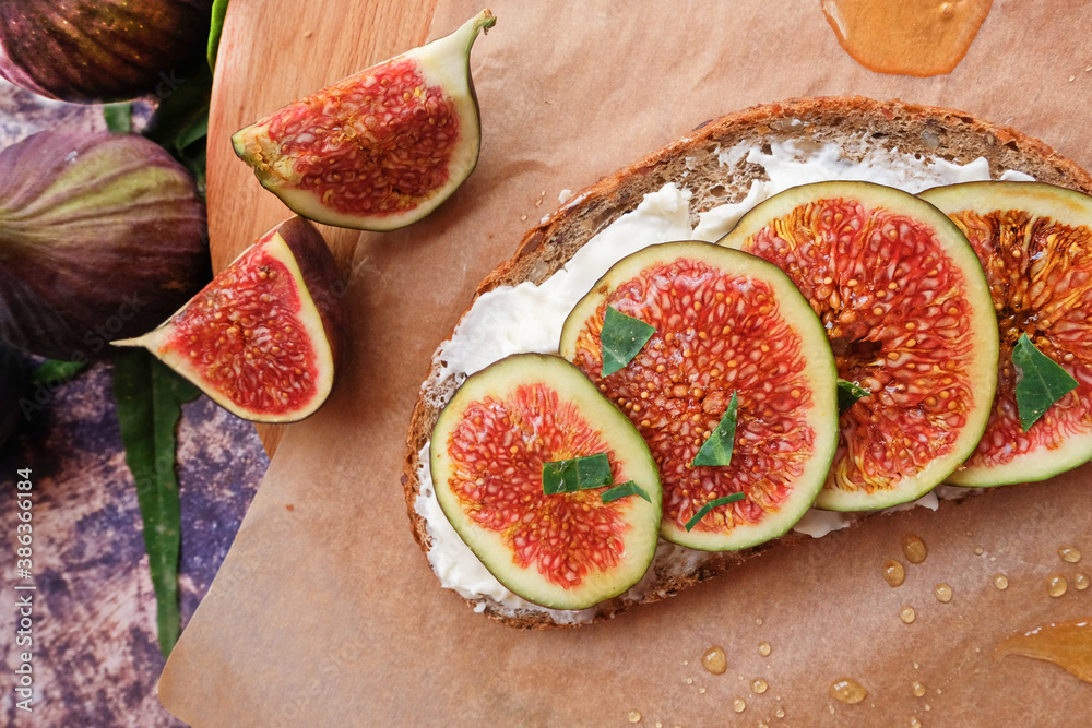 Figs. Sandwiches with figs, cheese, arugula, honey and nuts on wooden board over textured purple backdrop. Next to pieces of fresh figs with cinnamon. Homemade. Everyday autumn kitchen. Figs. Sandwiches with figs, cheese, arugula, honey and nuts on wooden board over textured purple backdrop. Next to pieces of fresh figs with cinnamon. Homemade. Everyday autumn kitchen.