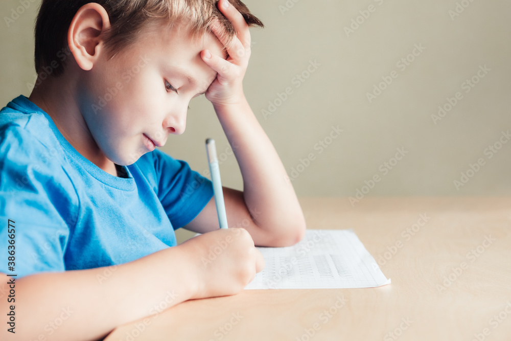 Side view to cute boy doing his homework. Child writing with pencil. Prewriting practice patterns as preparing hands for writing letters Side view to cute boy doing his homework. Child writing with pencil. Prewriting practice patterns as preparing hands for writing letters