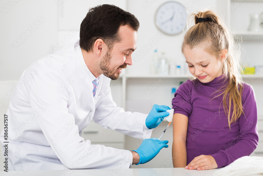 Fototapeta premium Young male doctor ready to make injection to teenage female visitor in hospital