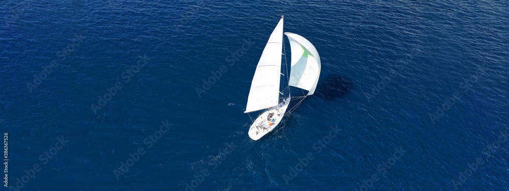 Aerial drone ultra wide panoramic photo of beautiful sailboat with white sails cruising deep blue sea near Mediterranean destination port