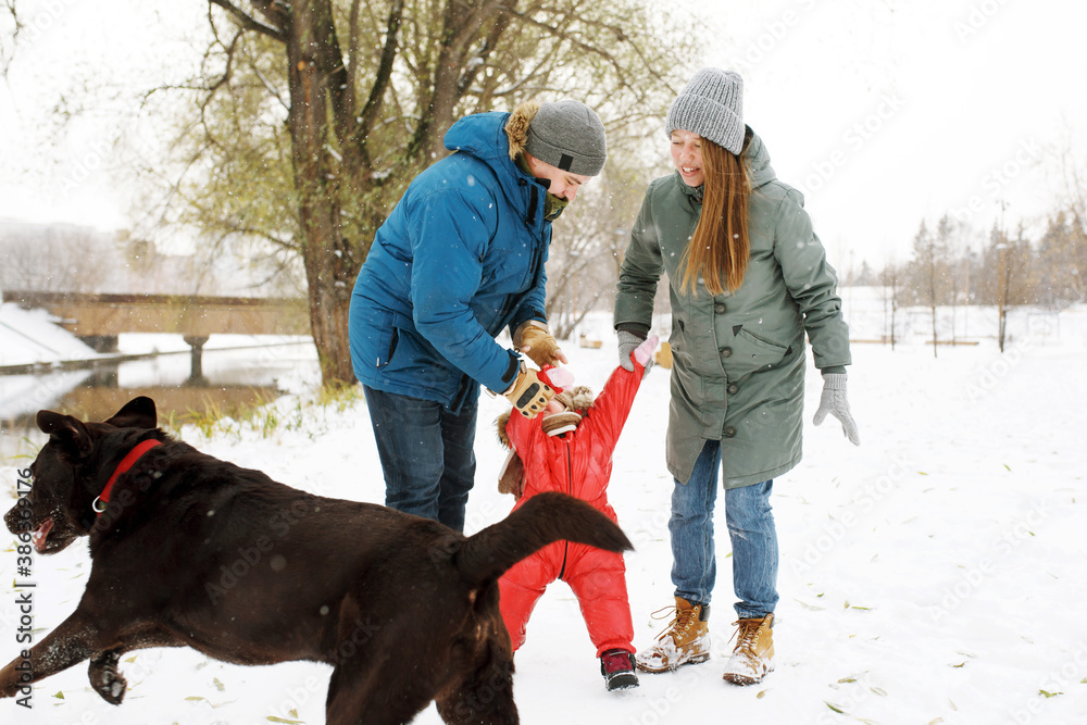 Full height of happy family with one naughty toddler and dog in winter casual oufit walking having fun outdoors
