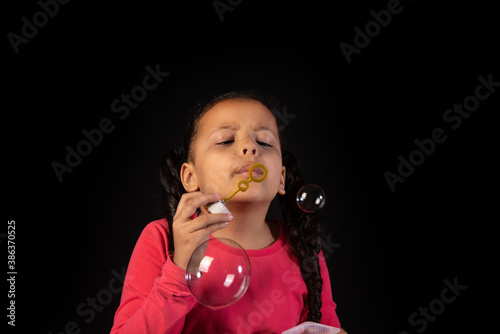 Brazilian girl with pink top playing soap bubbles, low key portrait, black background, selective focus.