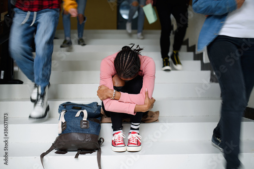 Depressed young student with face mask sitting on floor back at college or university, coronavirus concept. photo