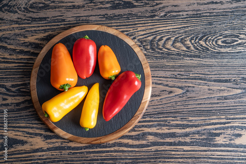 Colored mini peppers. Mixed sweet baby paprika or bell peppers on black plate and wooden table with text space. Top view