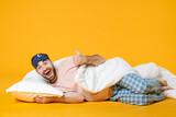 Full length of surprised excited cheerful man in pajamas home wear sleep mask lying showing thumb up isolated on bright yellow colour background studio portrait. Relax good mood lifestyle concept.